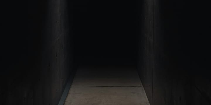 Dark concrete corridor with light in the foreground which gets dark quickly further away.